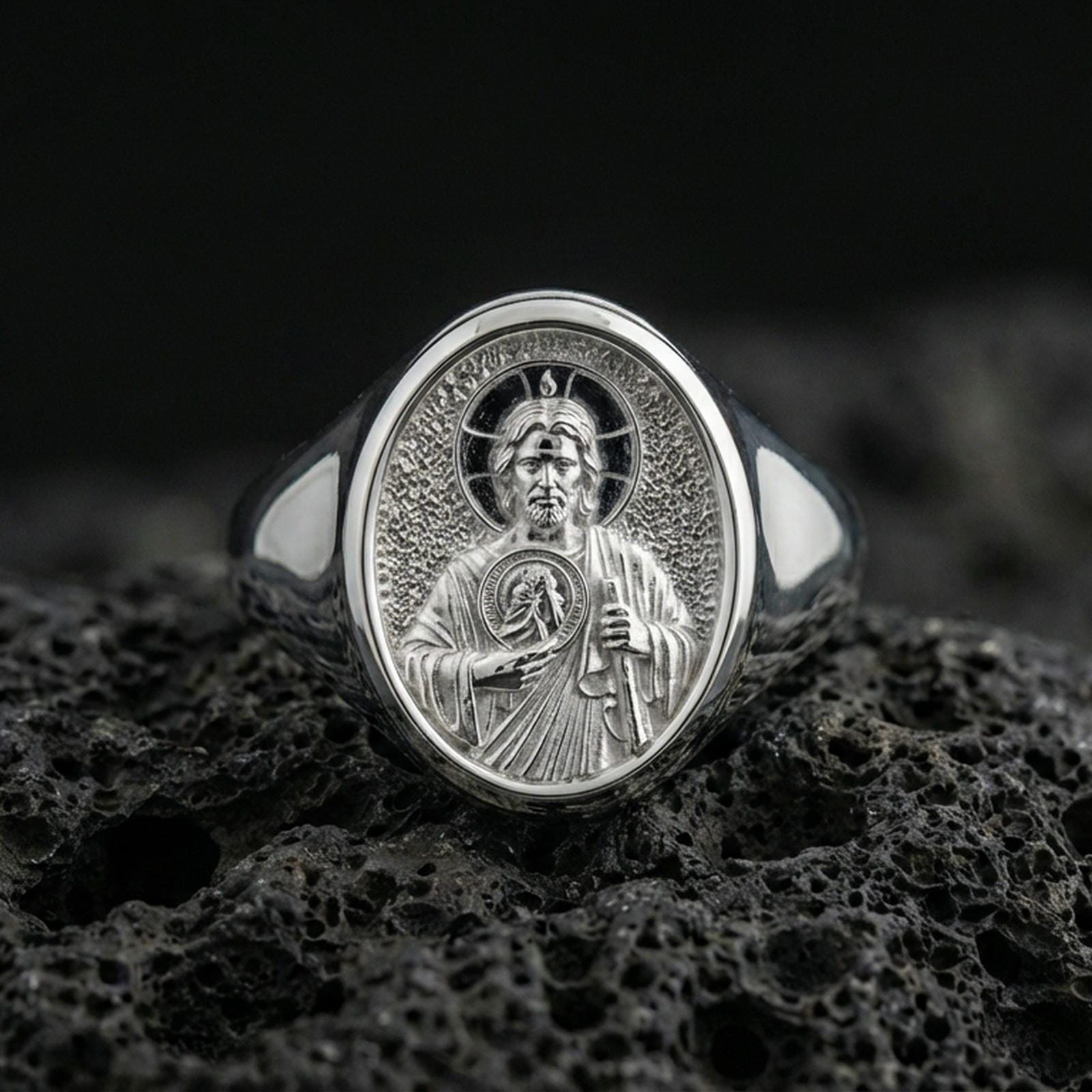 Polished silver Saint Jude ring on volcanic stone, detailed devotional signet closeup
