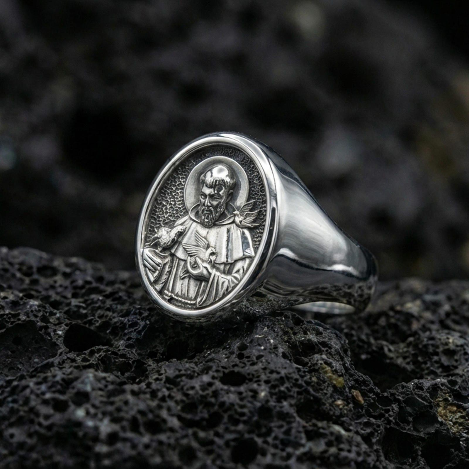 Polished silver St Francis ring on volcanic stone, Catholic devotional signet closeup