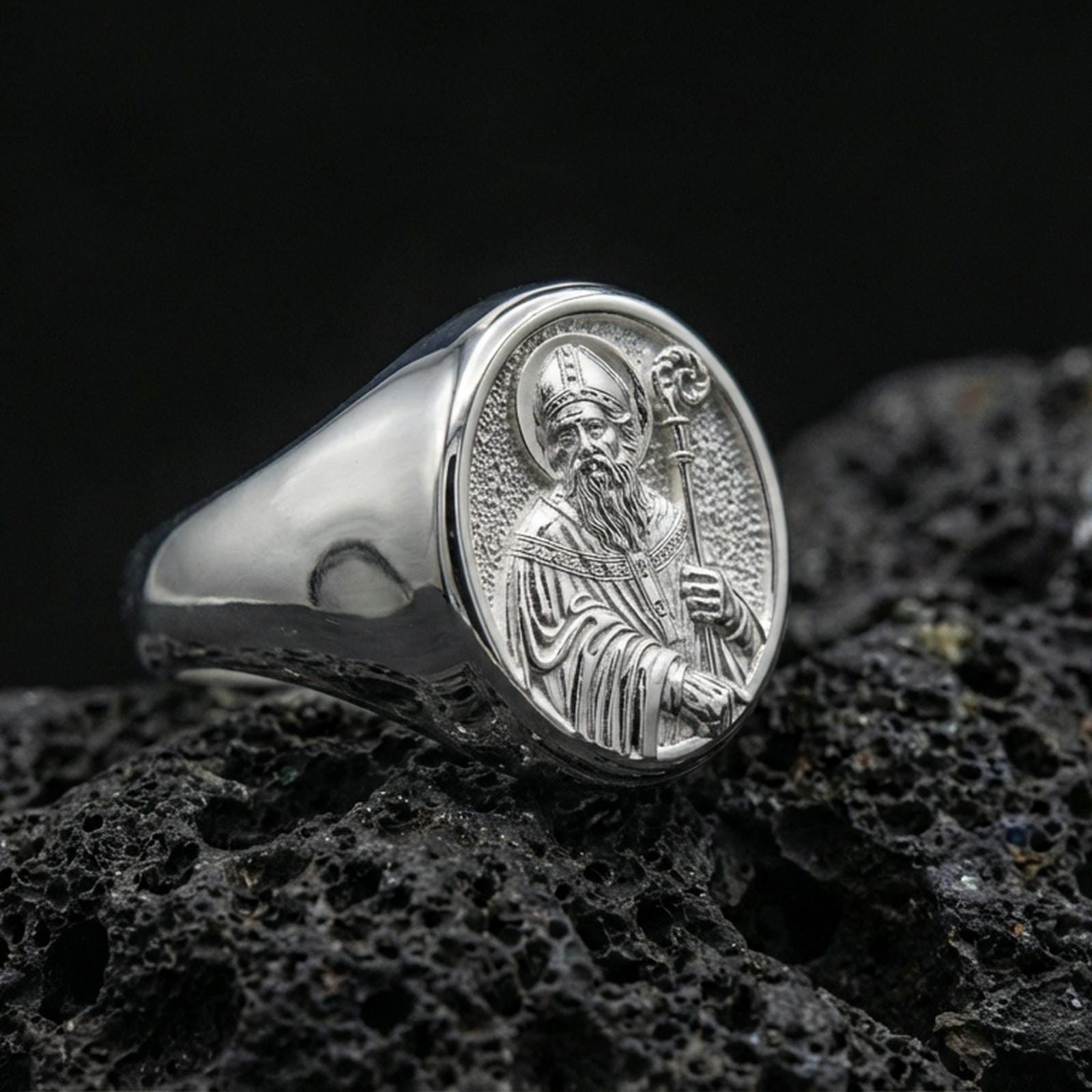 Polished silver Saint Benedict signet ring on porous volcanic stone, detailed saint engraving, religious signet ring