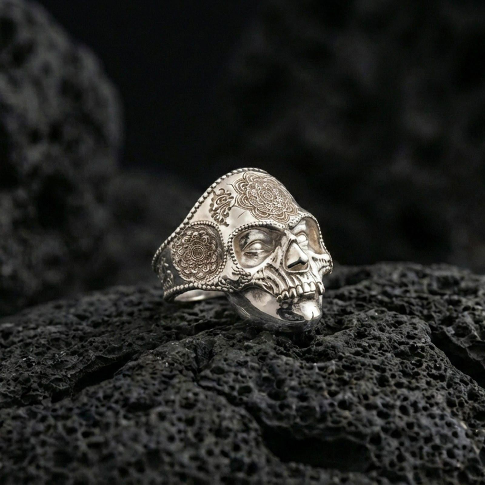 Polished silver skull mandala ring on porous volcanic stone, detailed floral engraving, biker gothic style