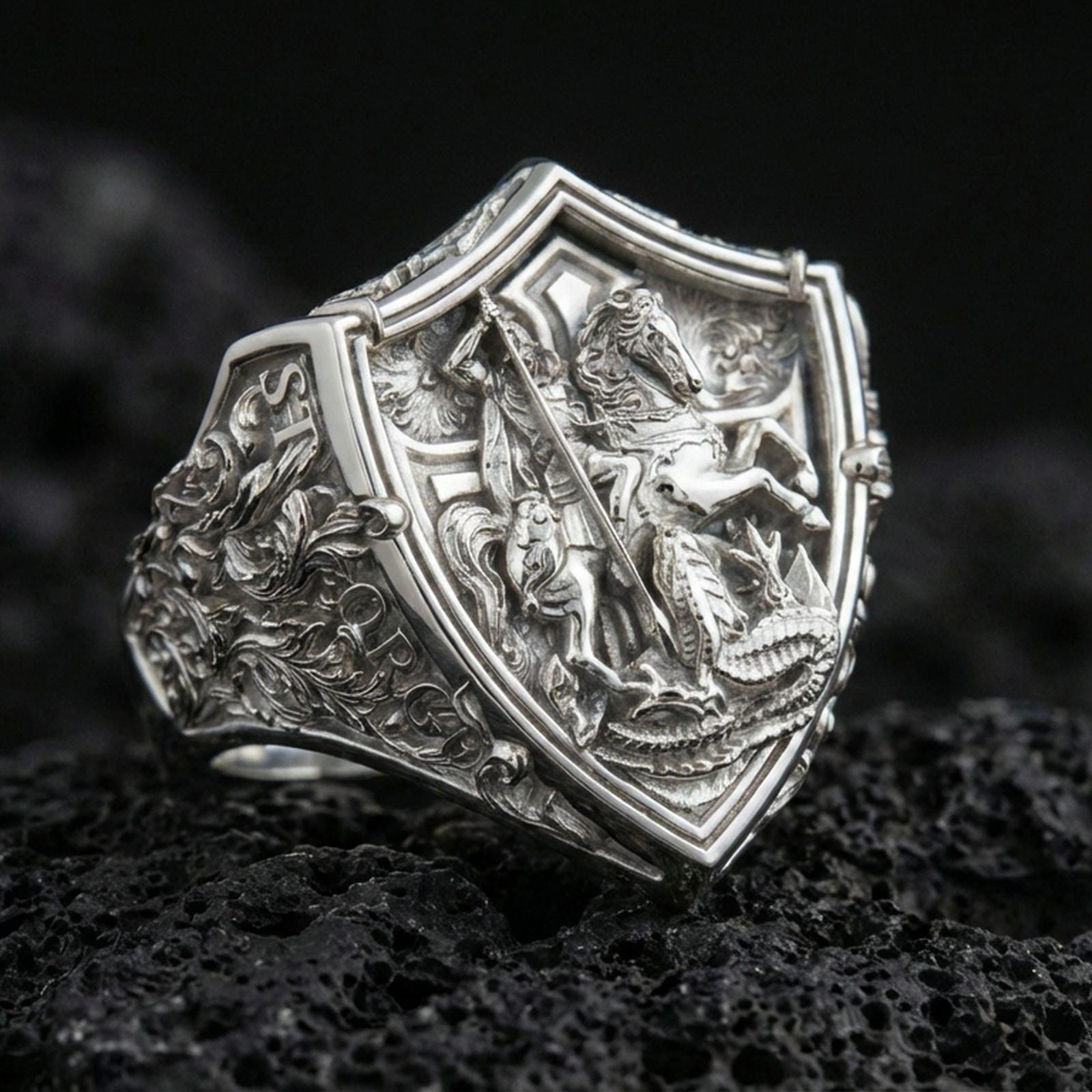 Polished silver Saint George and dragon shield ring on porous volcanic stone, detailed relief carving, statement signet style
