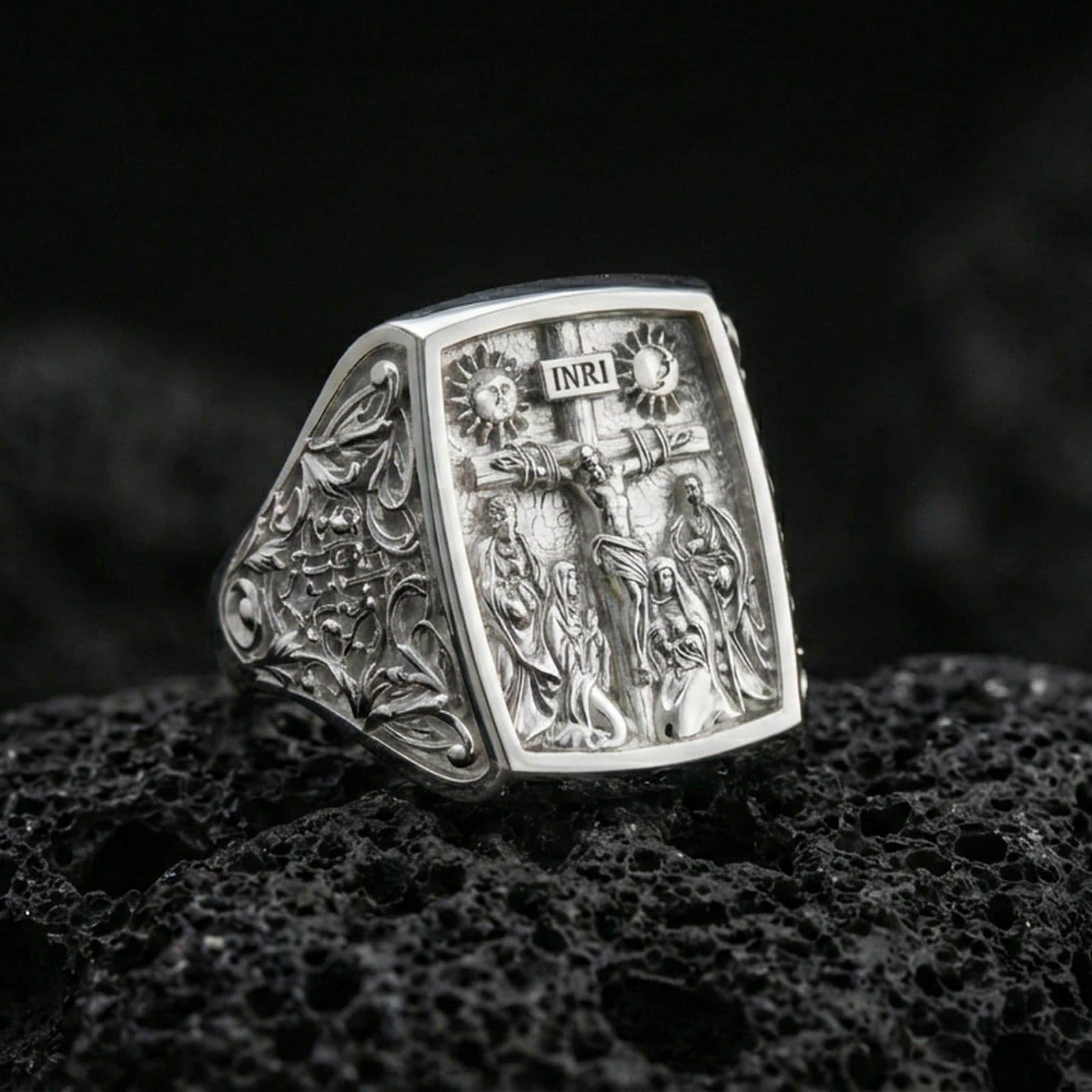 Polished silver INRI cross ring on porous volcanic stone, rectangular signet face with crucifixion scene, ornate side filigree