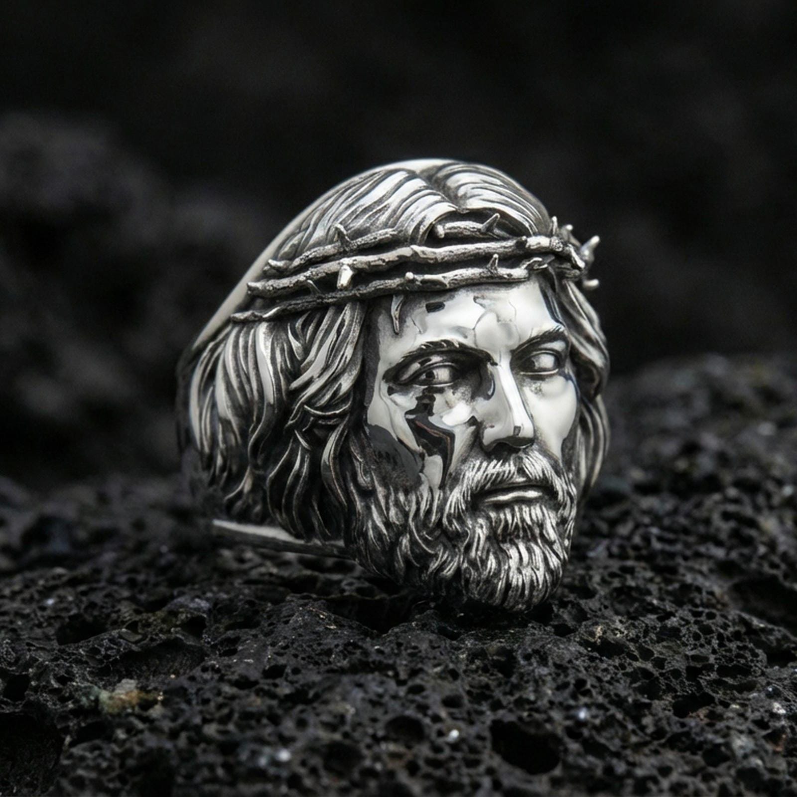 Polished silver Jesus crown of thorns ring on porous volcanic stone, detailed Christ face sculpt, bold Christian ring