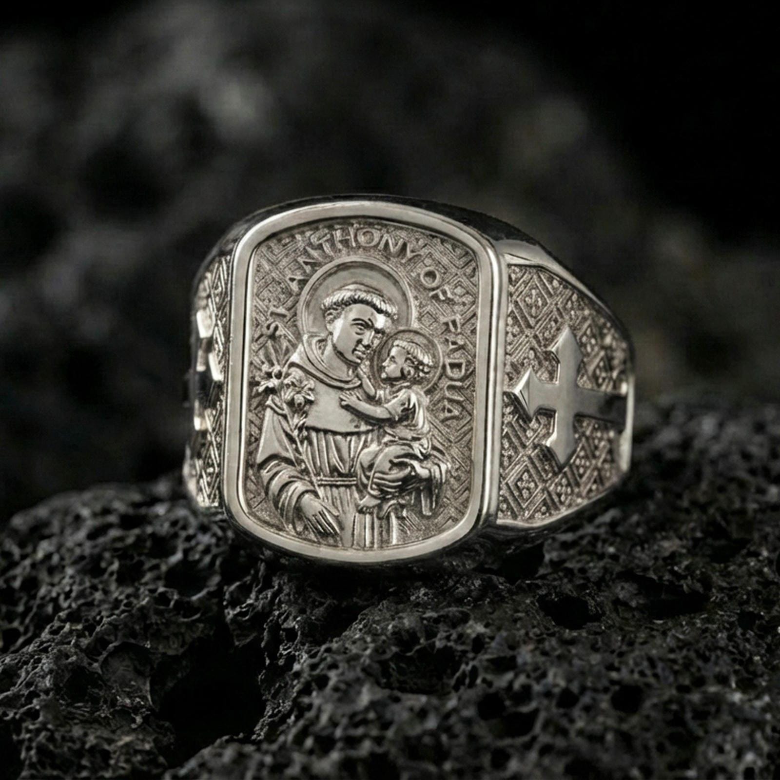 Polished silver Saint Anthony signet ring on porous volcanic stone, detailed saint relief and cross sides, Christian faith ring