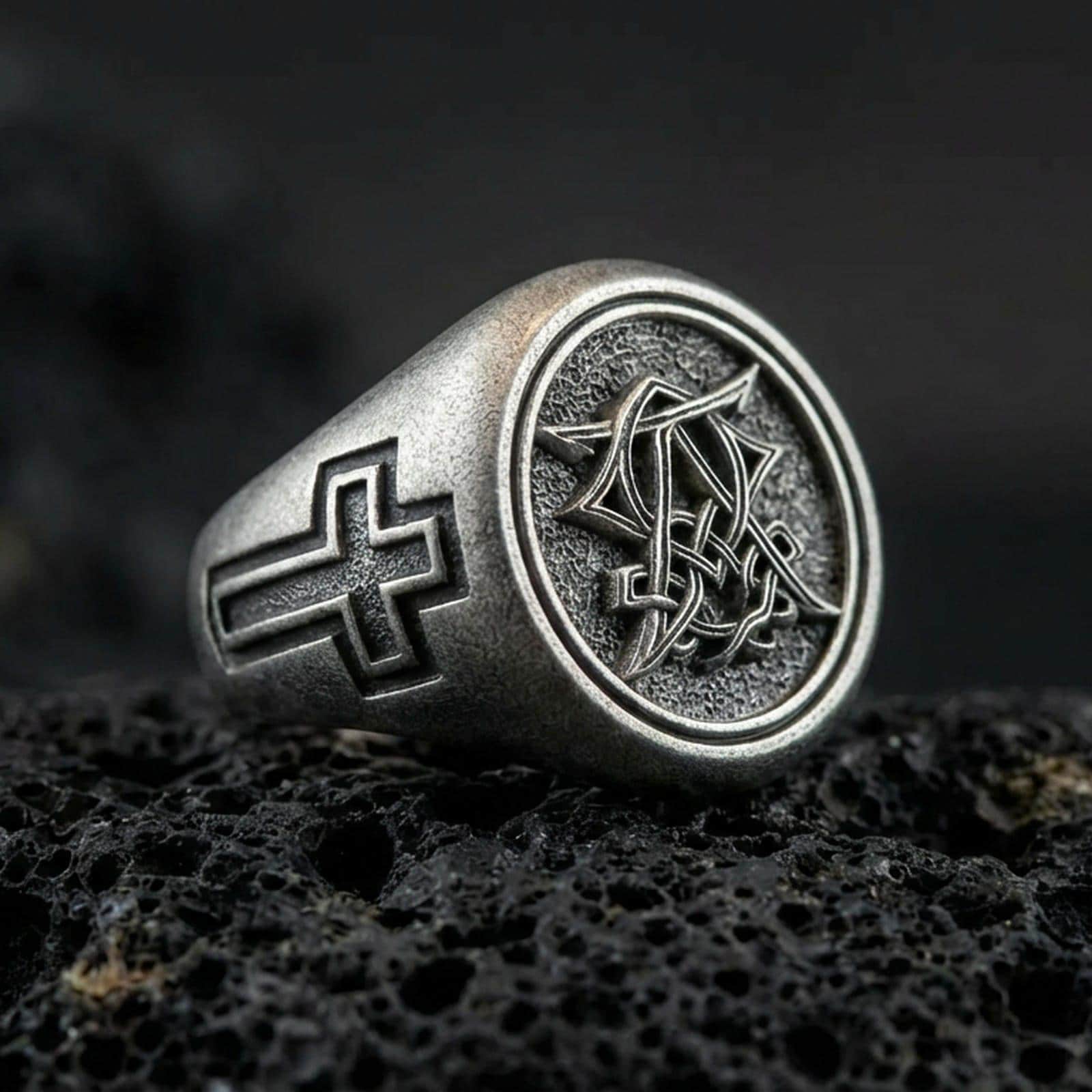 Oxidized 925 sterling silver Christian monogram signet ring on volcanic rock, cross-engraved band and intertwined letter emblem