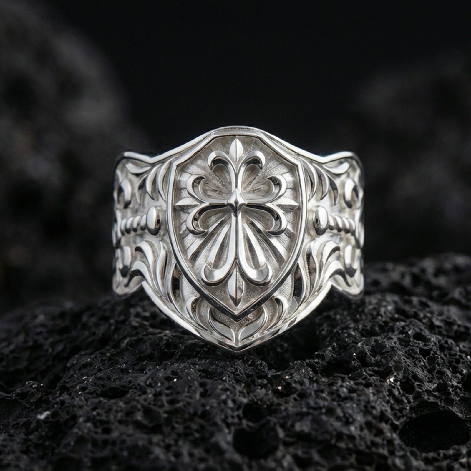 Polished silver heraldic cross shield signet ring on porous volcanic stone, raised shield crest and detailed scrollwork band