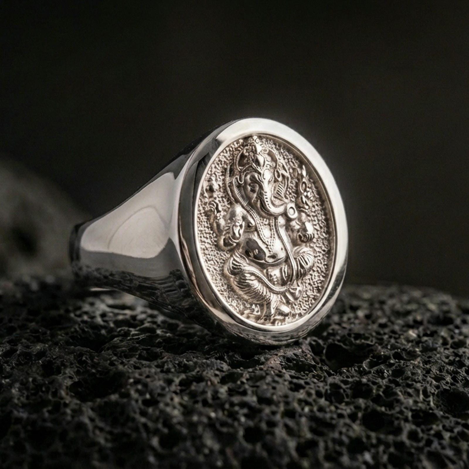 Polished silver Ganesha signet ring on porous volcanic stone, round face with engraved elephant god motif and smooth band