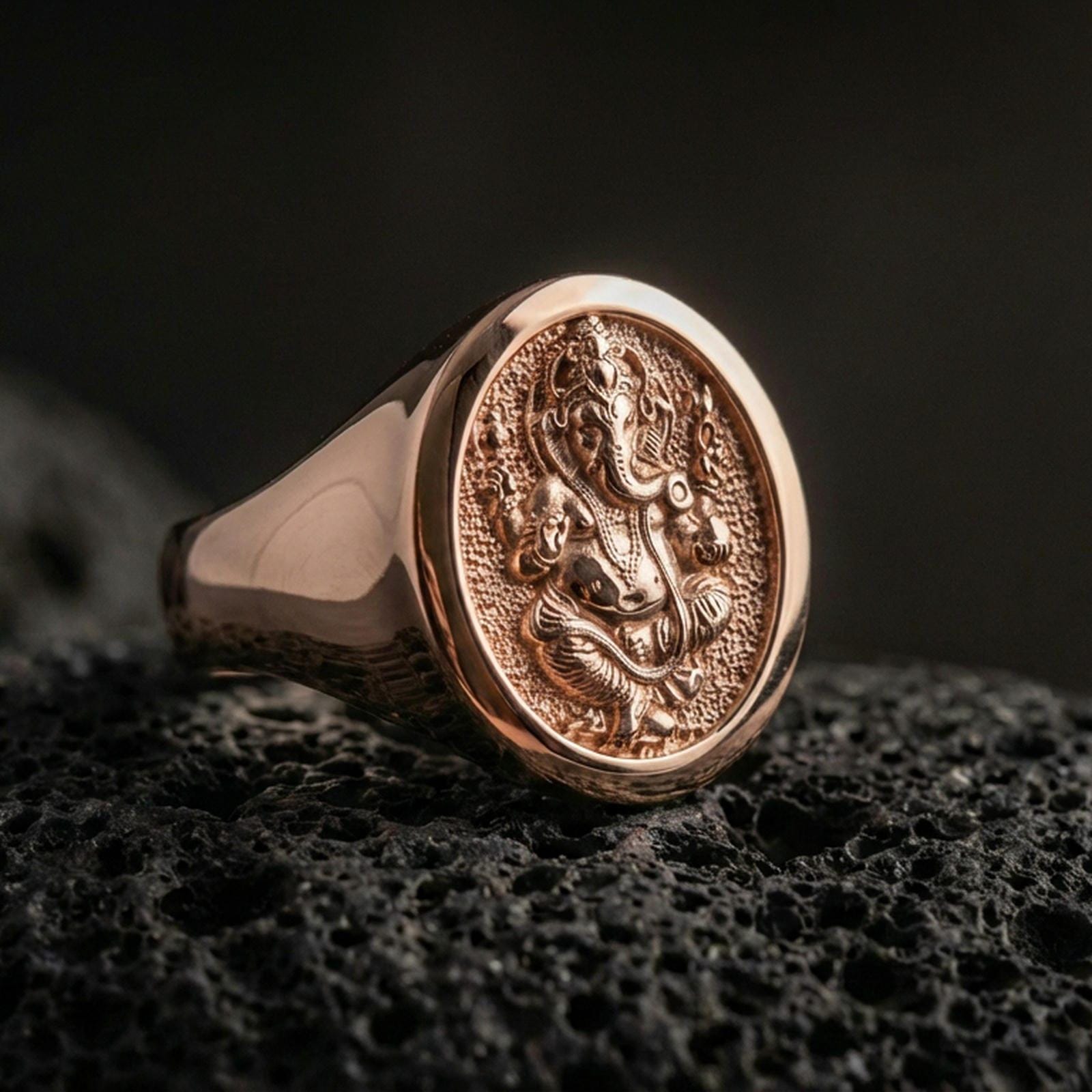 Rose gold plated Ganesha signet ring on volcanic stone, Hindu elephant god engraving with antique texture and thick signet profile