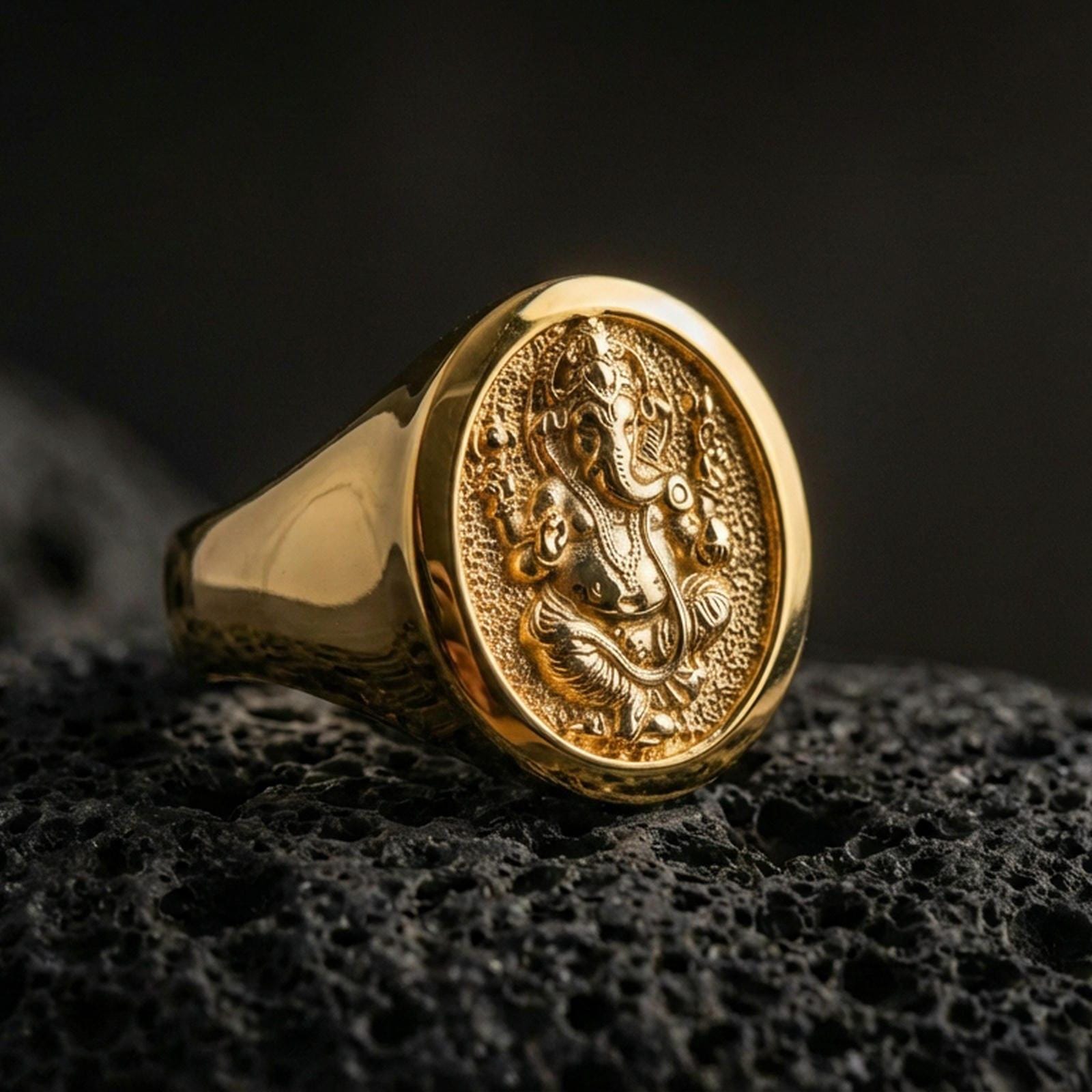 Gold plated Ganesha signet ring on dark volcanic rock, spiritual elephant deity design with raised relief and bold oval face