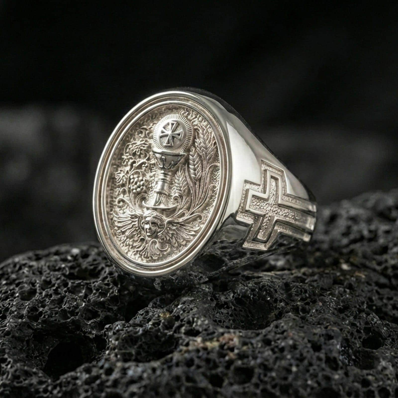 Polished silver Eucharist signet ring on porous volcanic stone, oval face with chalice, host, and ornate Christian scrollwork