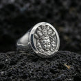 Load image into Gallery viewer, Polished silver spiritual signet ring on porous volcanic stone, oval face with multi-face deity motif and fine texture detail

