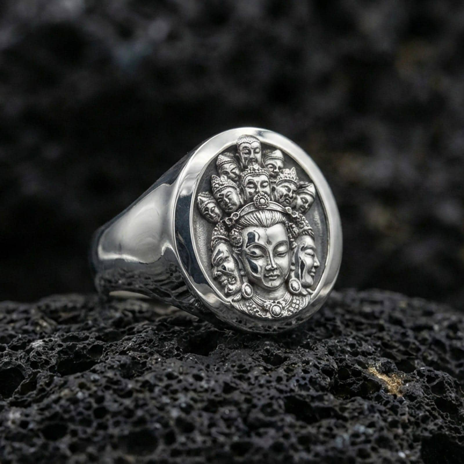 Polished silver spiritual signet ring on porous volcanic stone, oval face with multi-face deity motif and fine texture detail