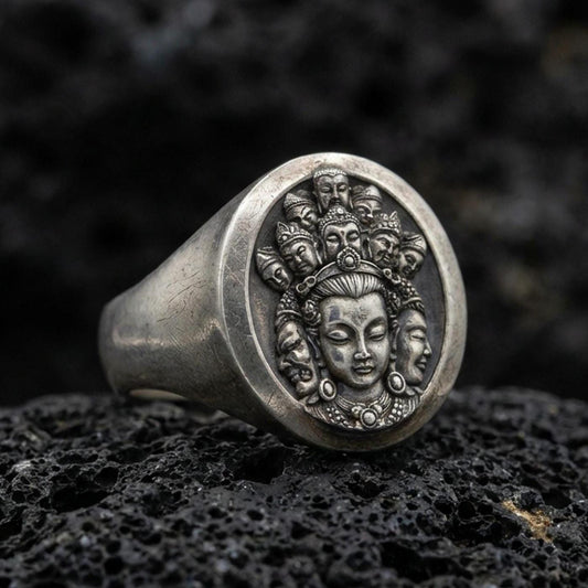 Oxidized 925 sterling silver multi-faced deity signet ring on volcanic rock, detailed Buddhist-inspired relief face engraving