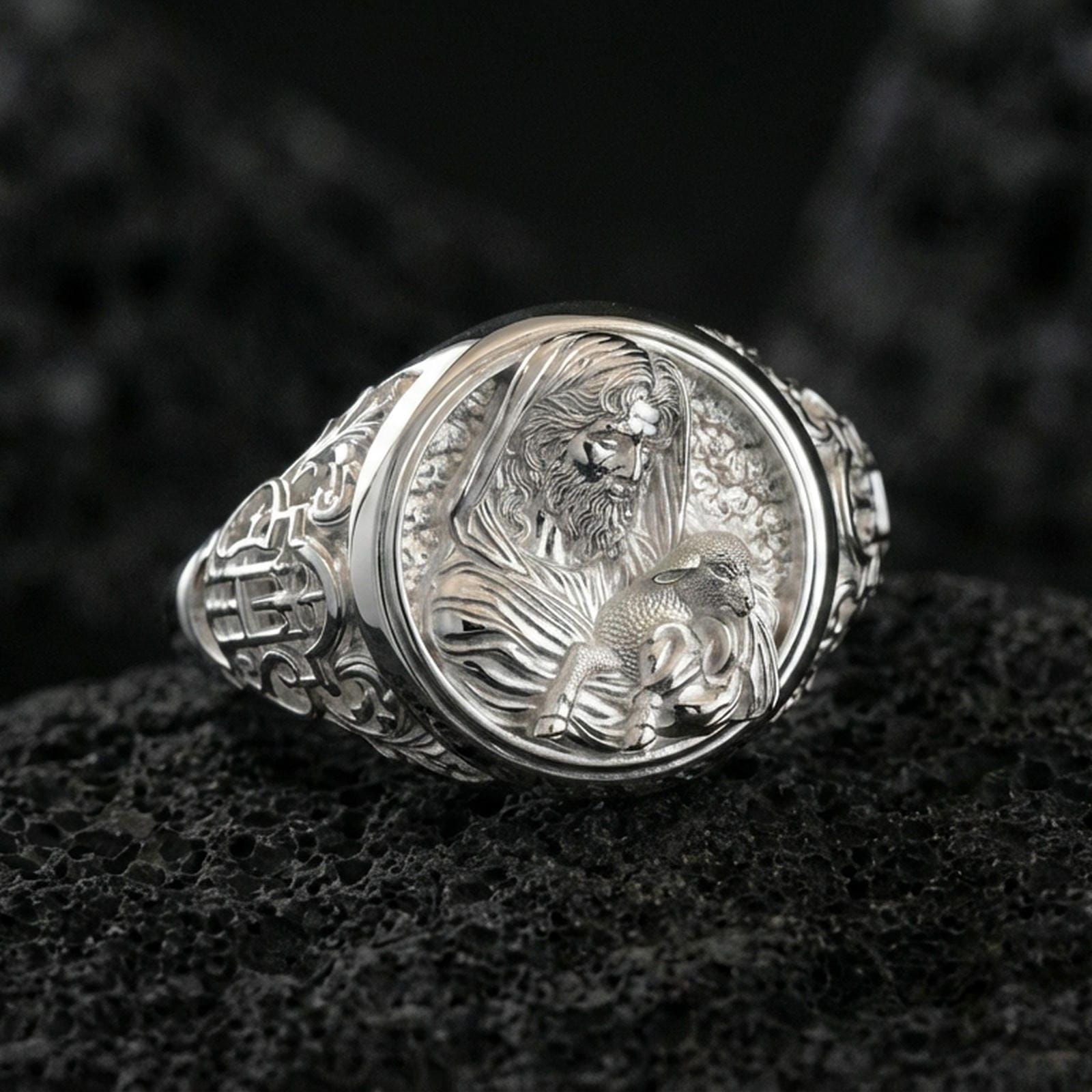 Polished silver Good Shepherd signet ring on porous volcanic stone, detailed Jesus and lamb engraving with smooth reflective frame