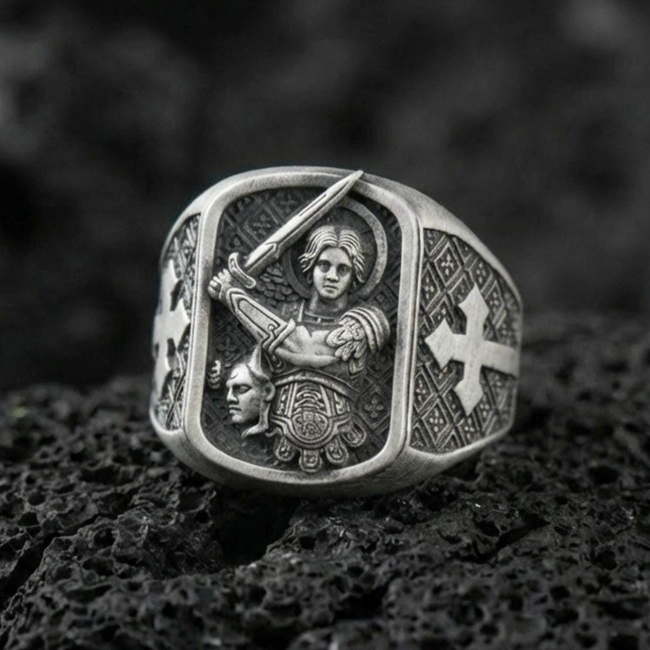 Oxidized Finish silver Saint Michael signet ring on porous volcanic stone, archangel with sword engraving, cross side detail close-up