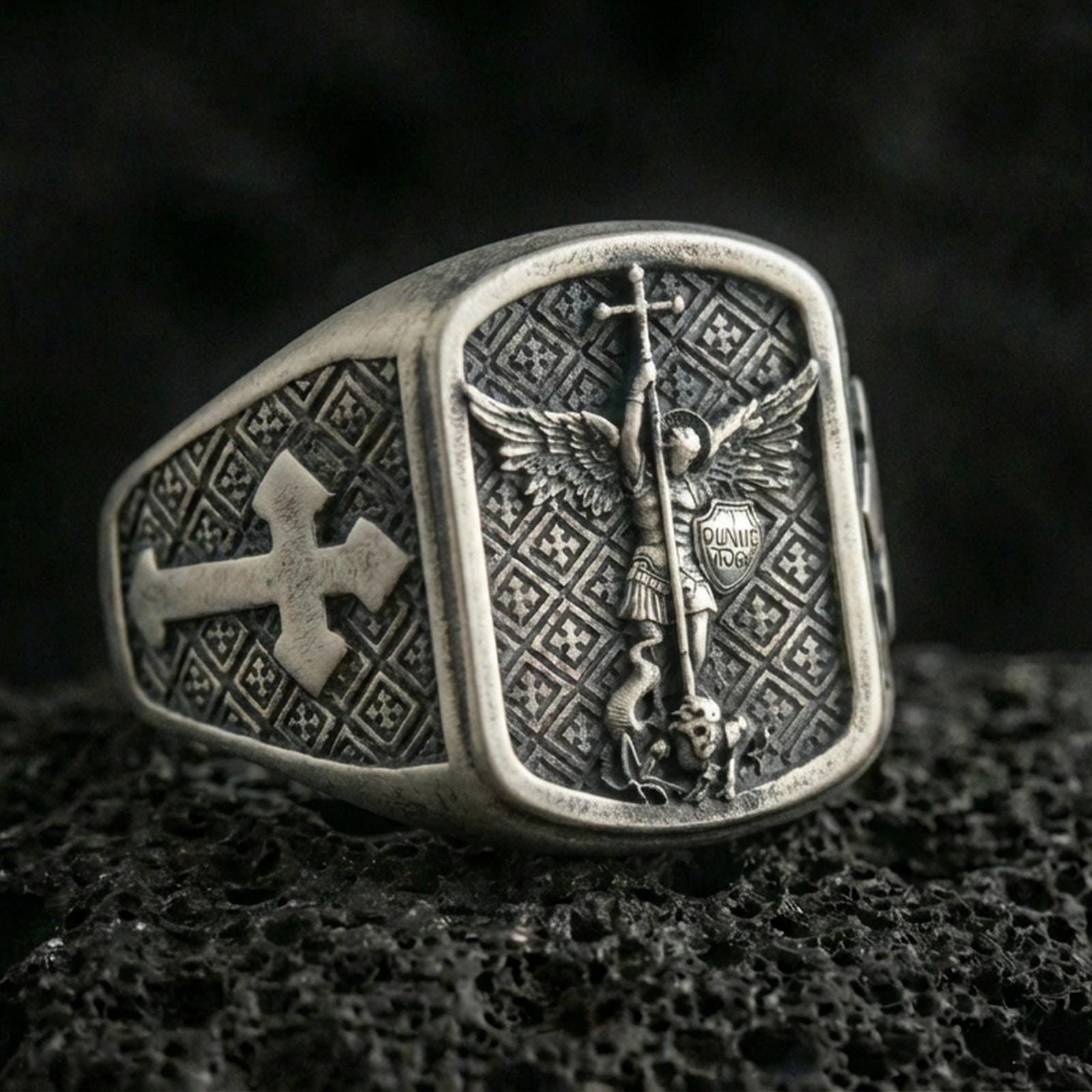 Oxidized 925 sterling silver Saint Michael ring on volcanic rock, archangel defeating devil relief with cross band