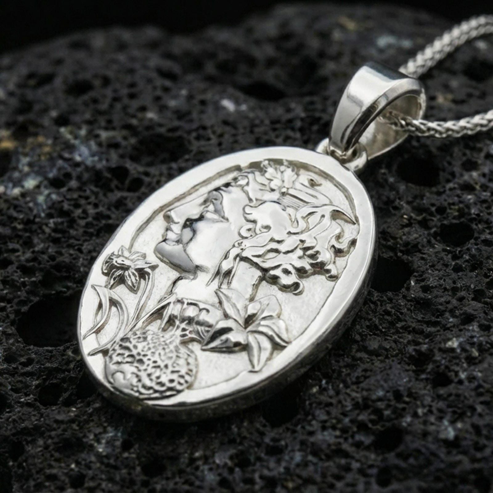 Polished silver Persephone pendant on porous volcanic stone, Greek goddess profile with pomegranate and floral relief necklace