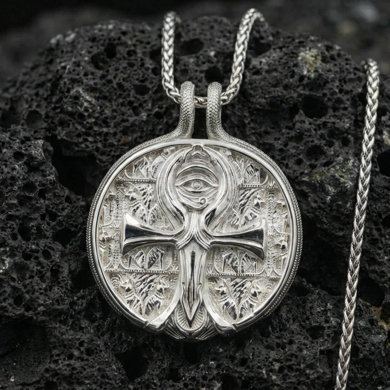 Polished silver ankh necklace on porous volcanic stone, Eye symbol medallion with detailed Egyptian-inspired relief and circular frame