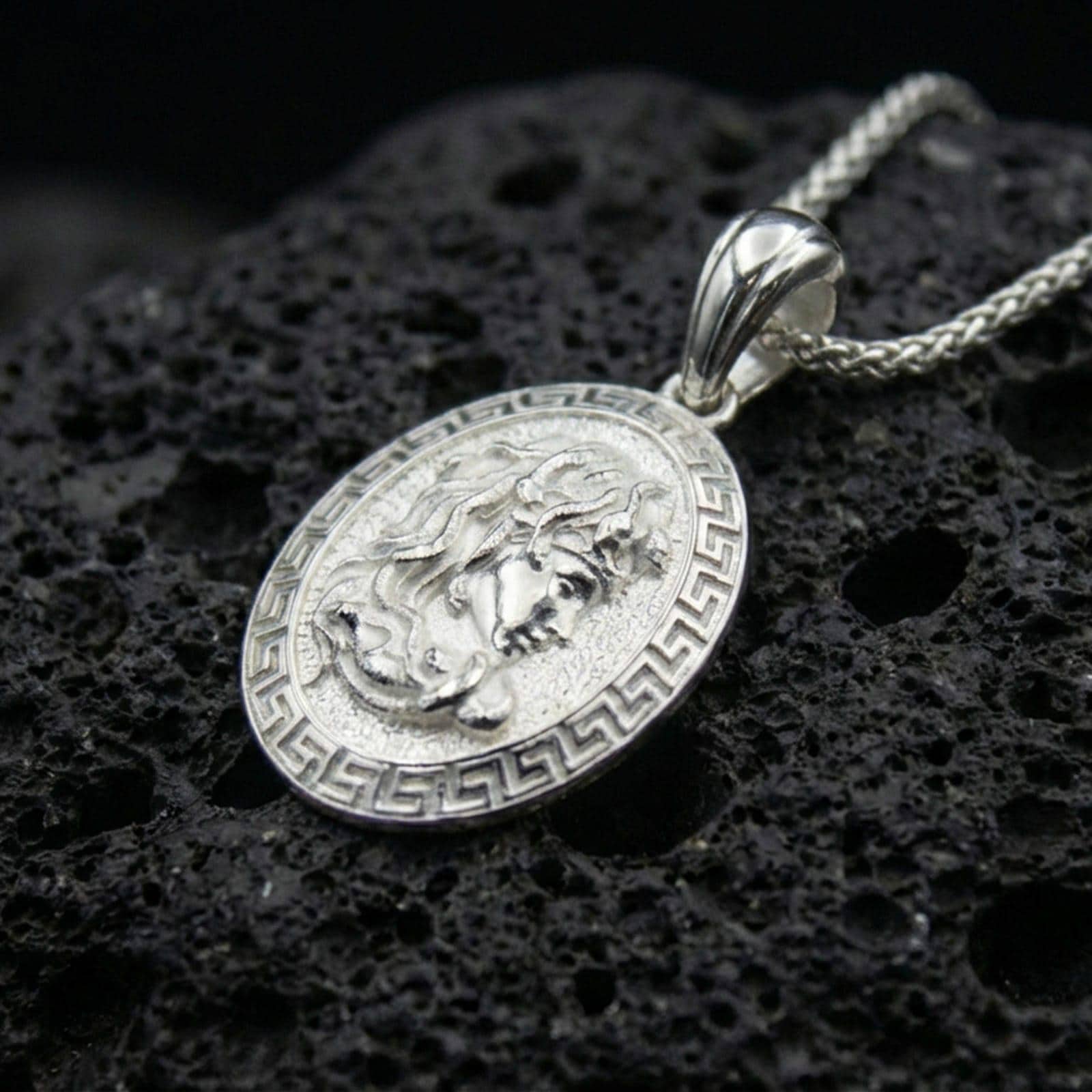 Polished silver Medusa necklace on porous volcanic stone, Greek key frame coin pendant with detailed relief portrait and vintage texture