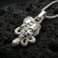 Load image into Gallery viewer, Polished silver Medusa skull necklace on porous volcanic stone, sculpted snake pendant with bold mythic face and high-detail texture

