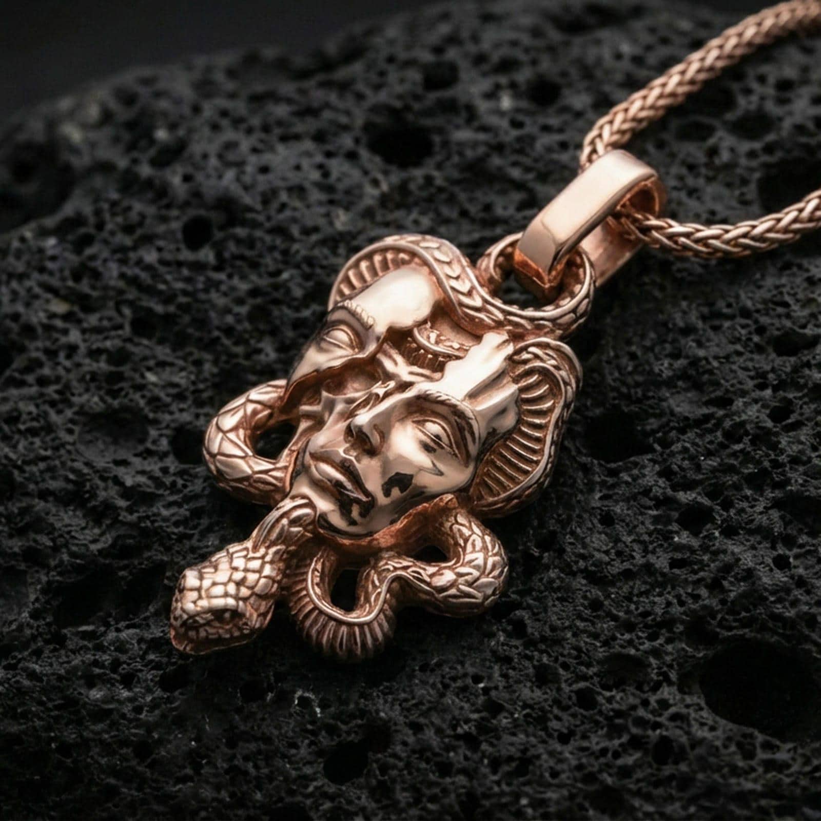 Rose gold plated Medusa skull necklace on dark volcanic stone, serpent-wrapped pendant with gothic myth design and premium shine