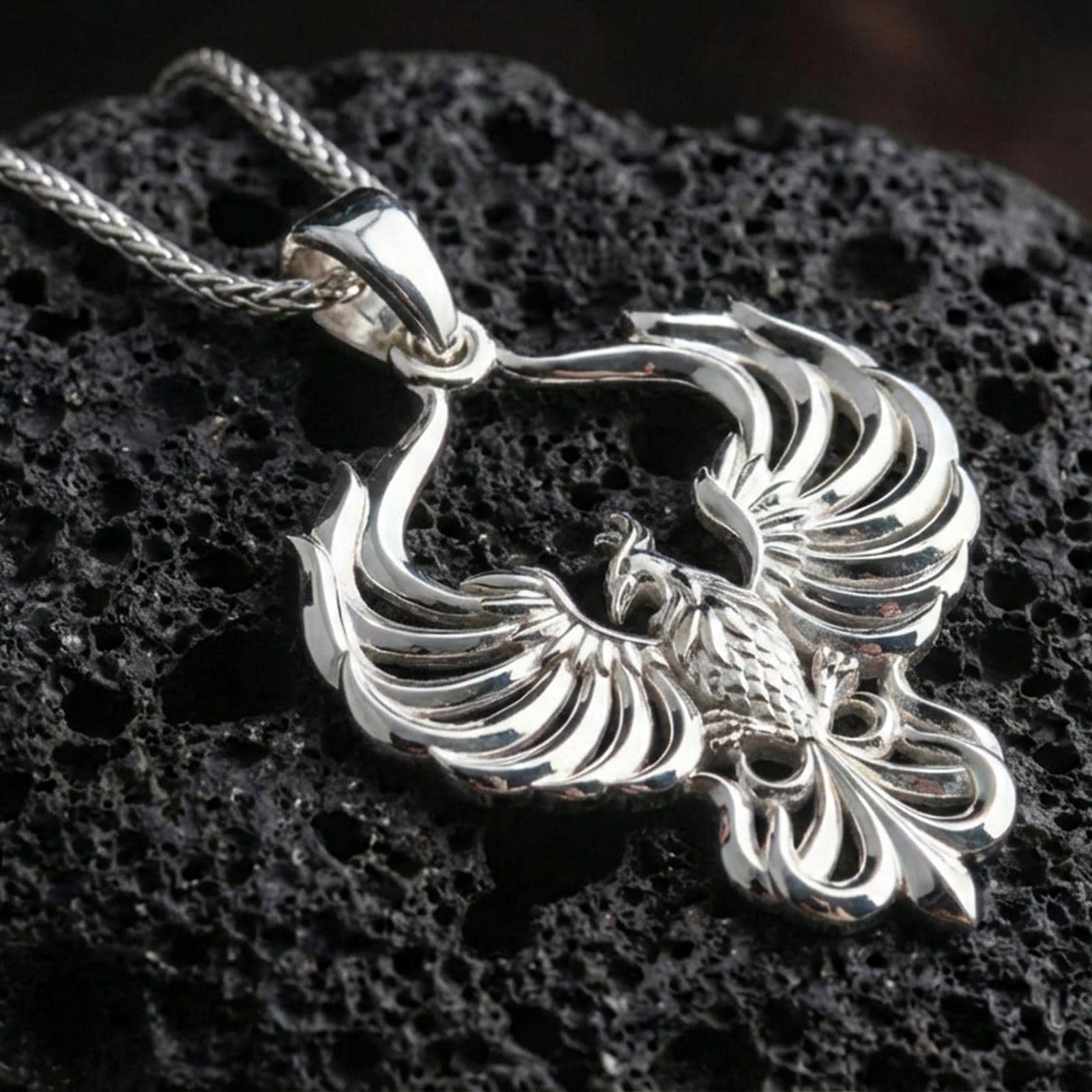 Polished silver phoenix necklace on porous volcanic stone, rising bird pendant with clean satin highlights and depth