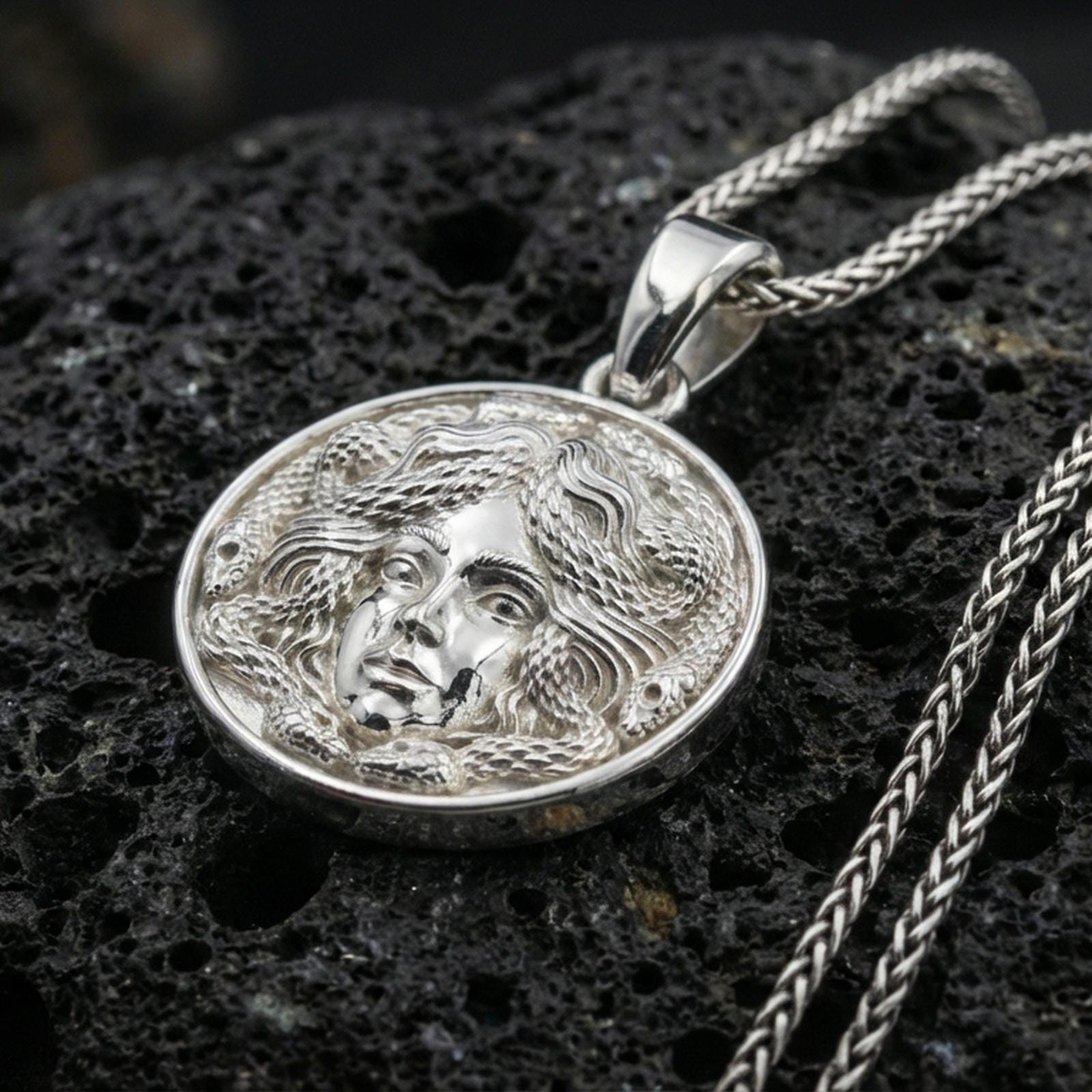 Polished silver medusa coin necklace on porous volcanic stone, detailed gorgon face medallion with crisp sculpting