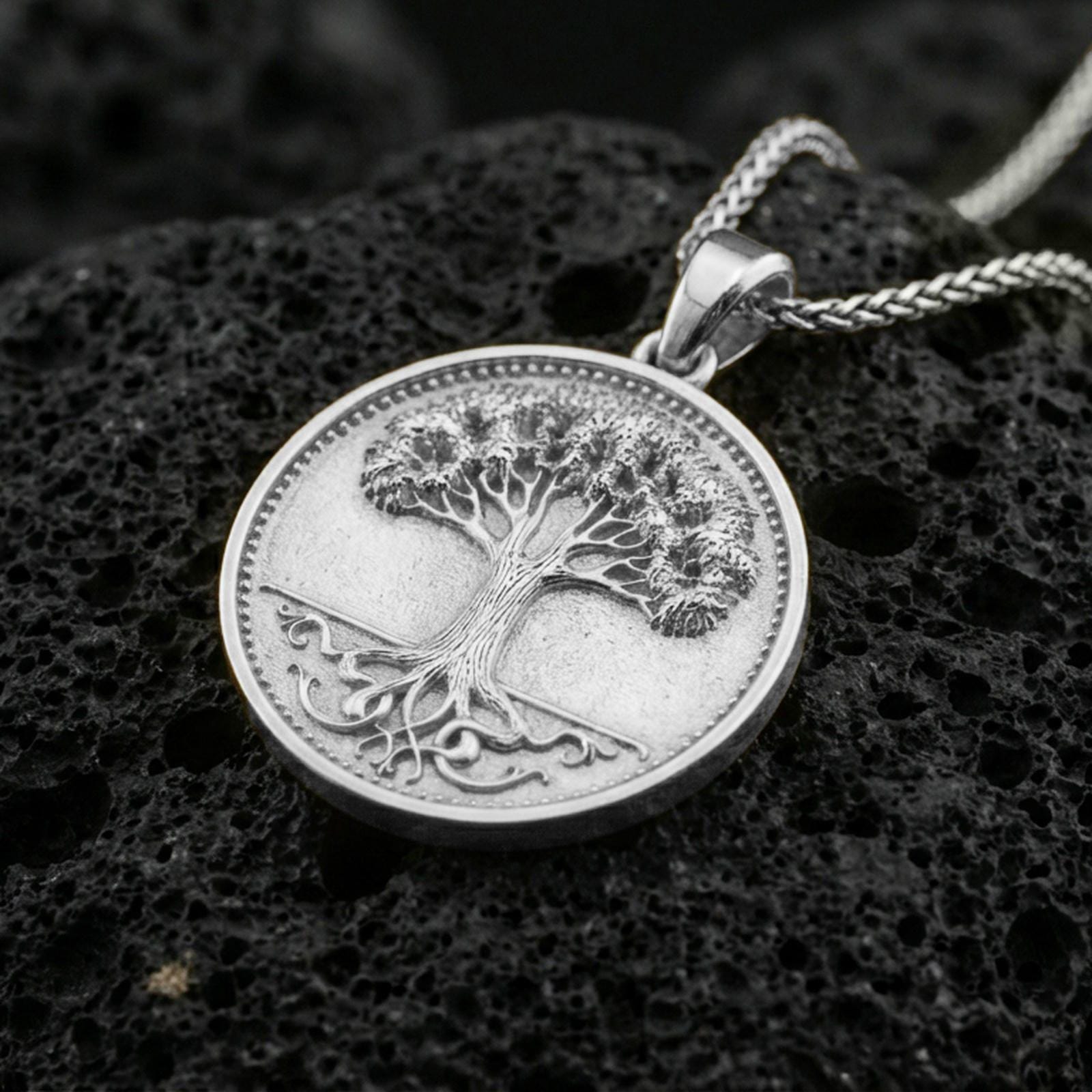 Polished silver Tree of Life medallion on porous volcanic stone, round coin pendant with detailed bark texture