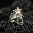 Load image into Gallery viewer, Polished silver open skull ring on porous volcanic stone, close-up highlighting smooth reflective edges and carved grain detailing
