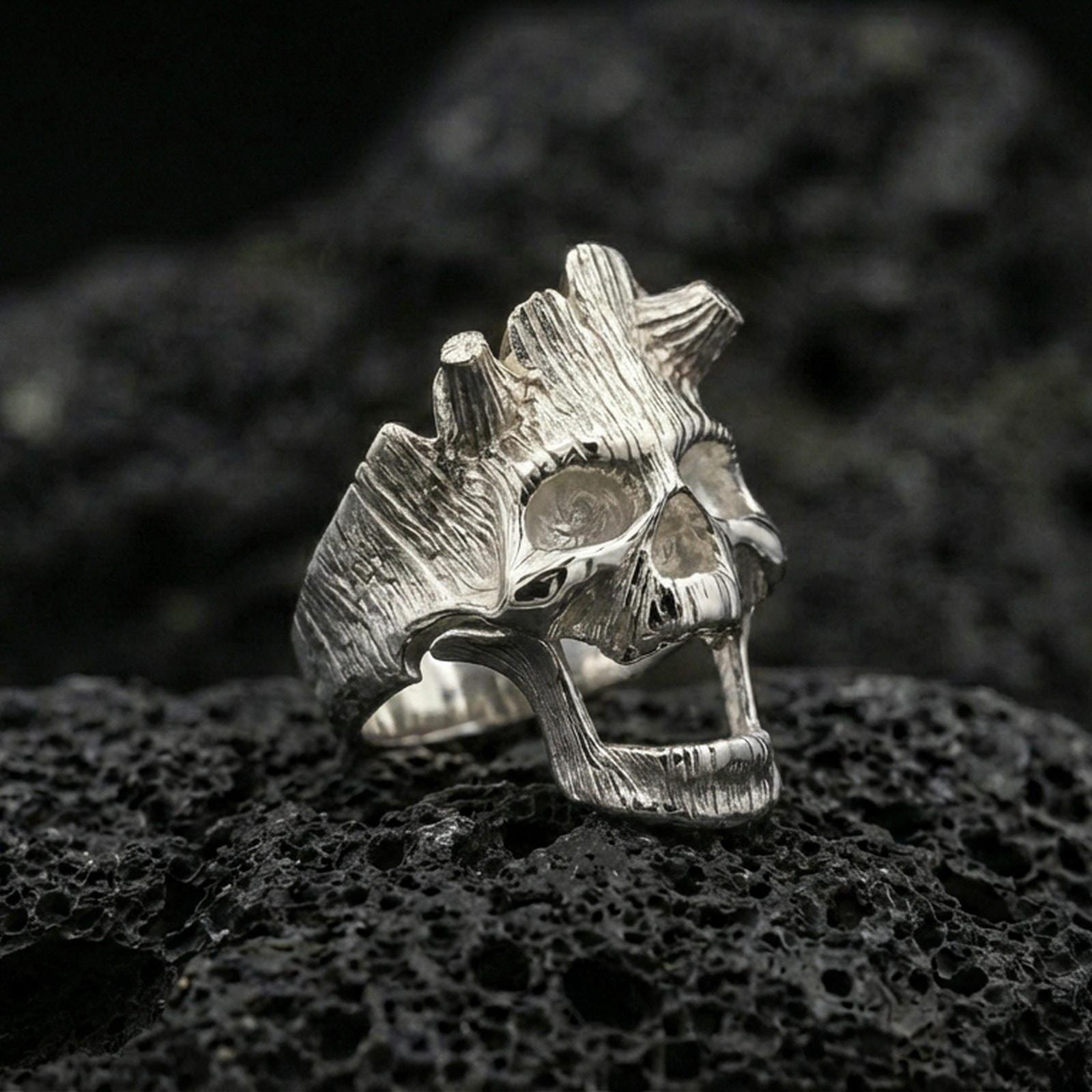 Polished silver open skull ring on porous volcanic stone, close-up highlighting smooth reflective edges and carved grain detailing