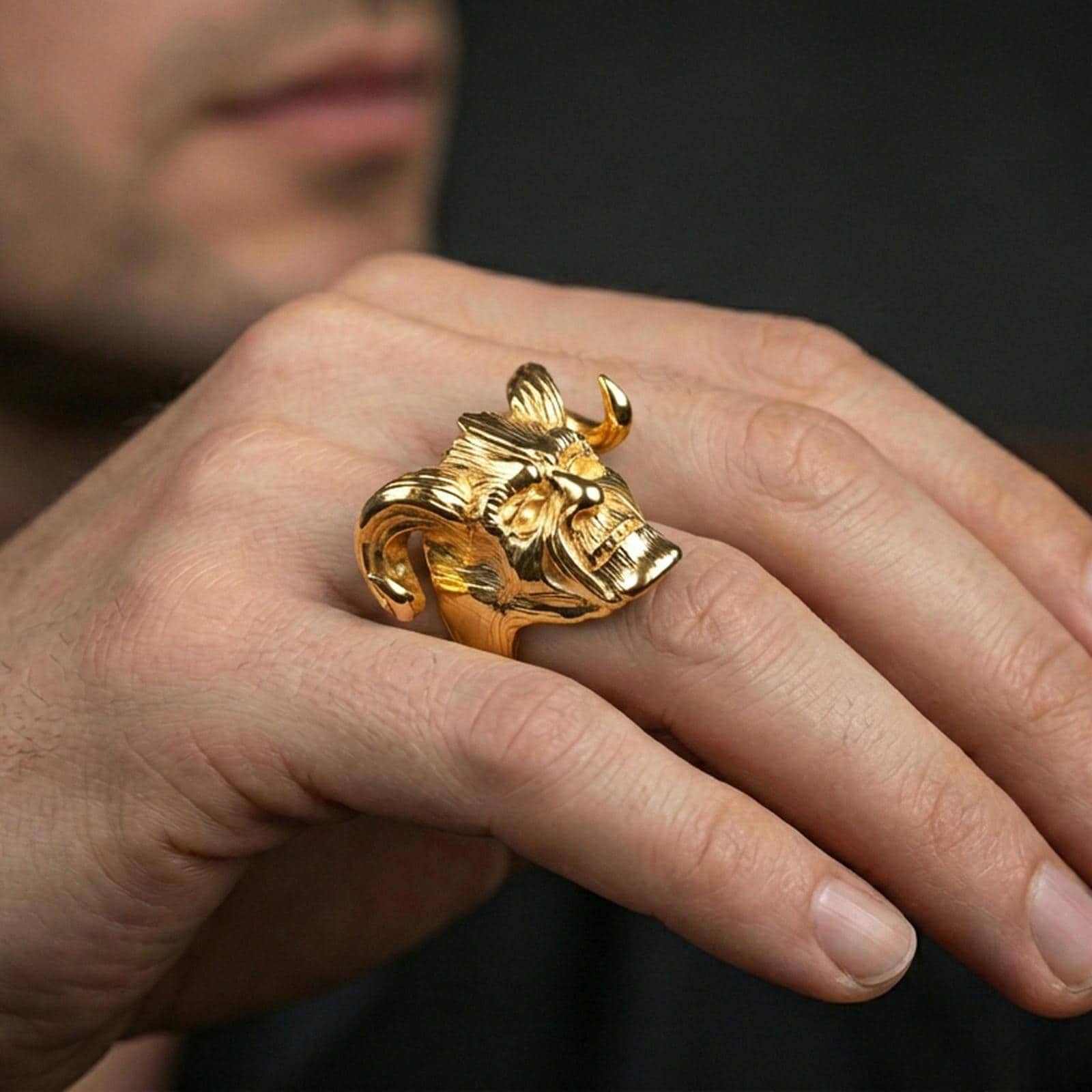 Gold plated horned skull statement ring worn on a finger, lifestyle image emphasizing bright plating tone and bold fantasy skull design
