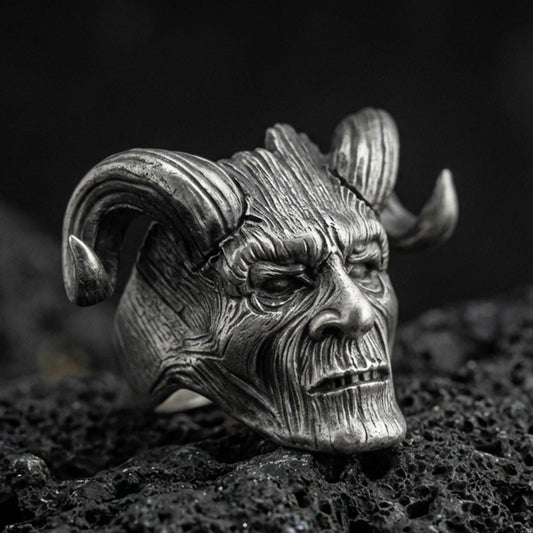 Oxidized sterling silver horned skull ring on black volcanic rock, macro close-up showing carved wood-grain texture and deep shadowed details
