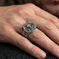 Load image into Gallery viewer, Oxidized Viking skull helmet ring worn on a finger, lifestyle close-up showing the wide band, carved knotwork borders and crossed axes emblem
