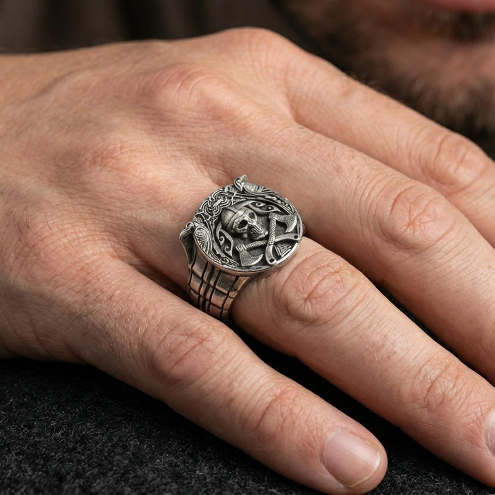 Oxidized Viking skull helmet ring worn on a finger, lifestyle close-up showing the wide band, carved knotwork borders and crossed axes emblem