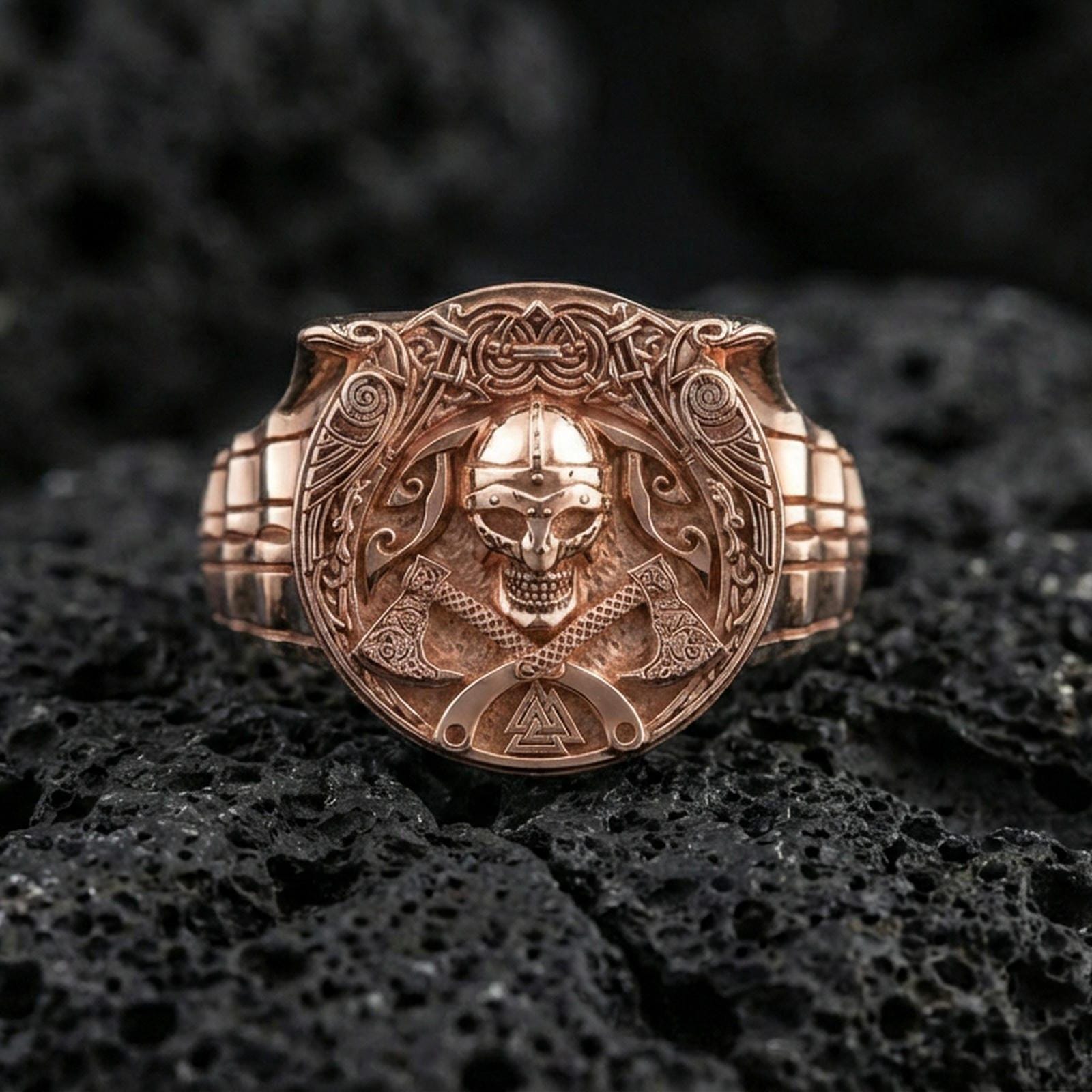 Rose gold plated Viking warrior ring on textured volcanic rock, luxury close-up capturing warm tone, intricate knotwork frame and skull helmet centerpiece