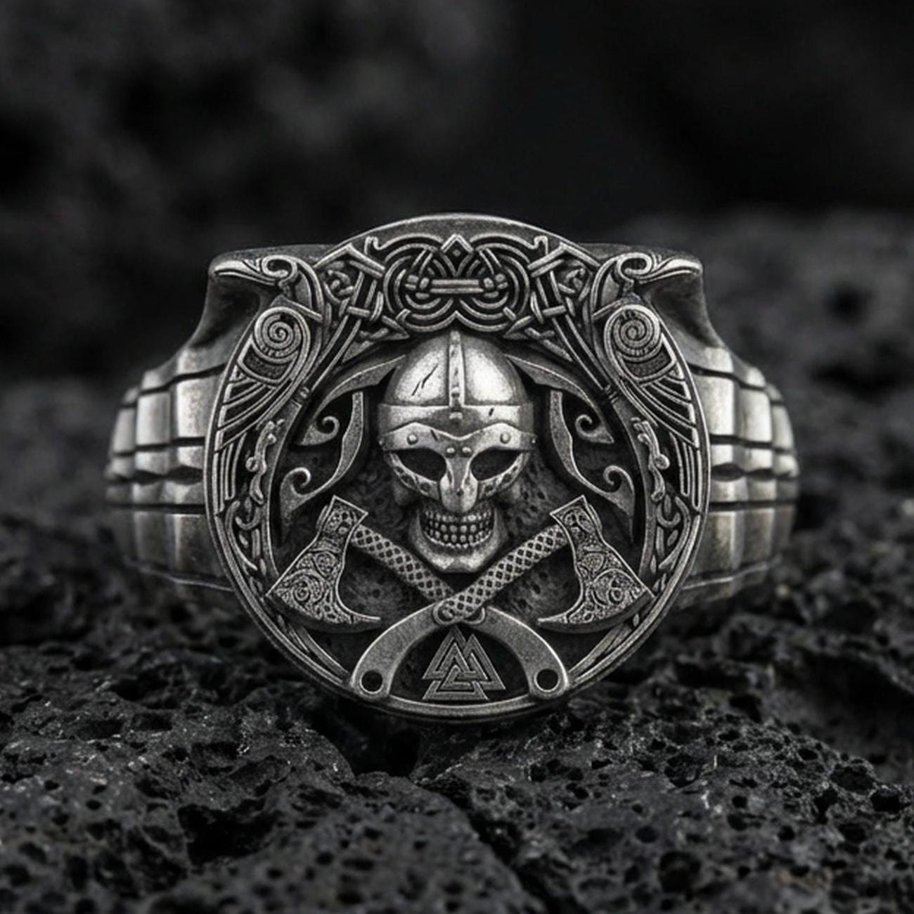 Oxidized sterling silver Viking warrior ring on black volcanic rock, macro close-up showing skull helmet relief, crossed axes and deep shadowed engravings