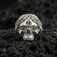 Load image into Gallery viewer, Polished silver Roman laurel skull ring on porous volcanic stone, close-up highlighting the leaf crown sculpting and crisp skull contours
