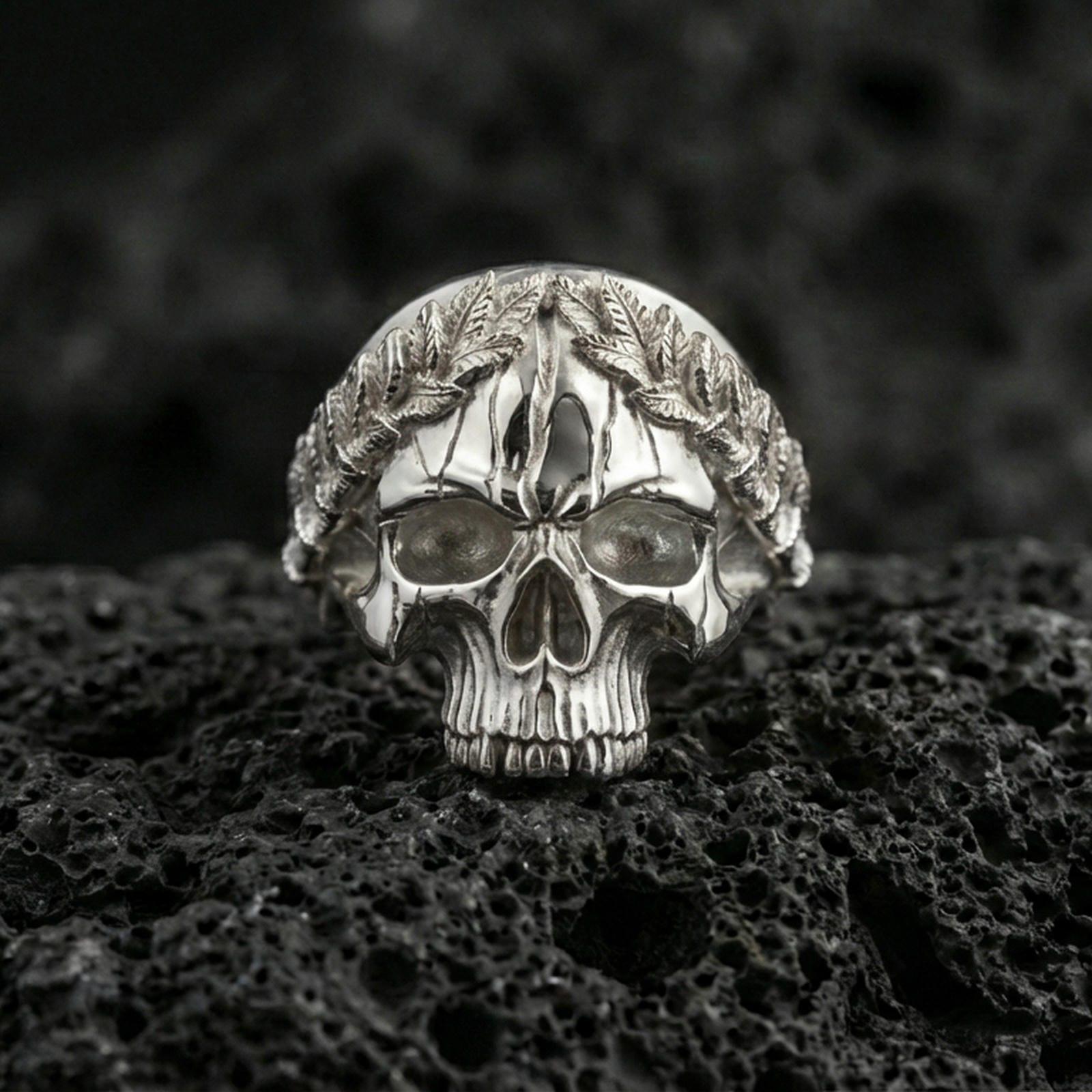 Polished silver Roman laurel skull ring on porous volcanic stone, close-up highlighting the leaf crown sculpting and crisp skull contours