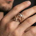 Load image into Gallery viewer, Rose gold plated skull ring with skeletal hand worn on a finger, close-up lifestyle image showcasing warm finish, detailed bone texture and gothic character
