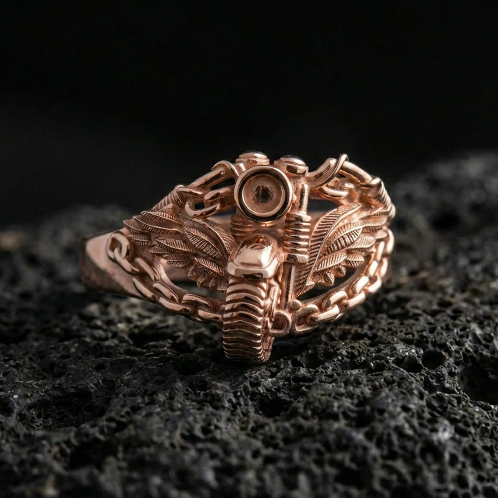 Rose gold plated motorcycle wing ring with chain band on textured volcanic rock, luxury close-up capturing warm plating glow and high-relief mechanical detailing