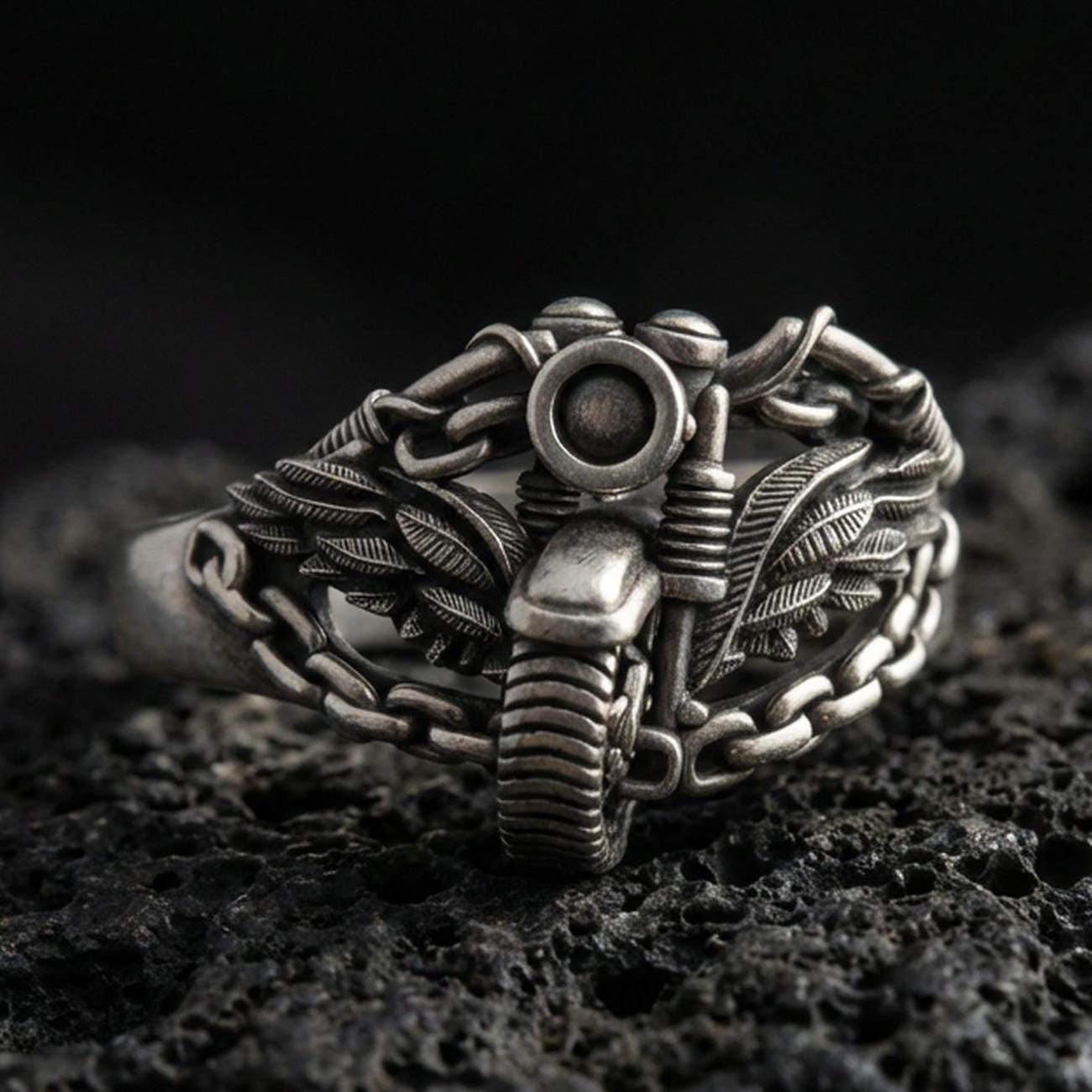 Oxidized sterling silver motorcycle ring with winged chain design on black volcanic rock, macro close-up highlighting darkened grooves and industrial biker detail