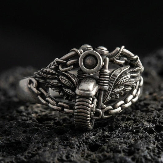 Oxidized sterling silver motorcycle ring with winged chain design on black volcanic rock, macro close-up highlighting darkened grooves and industrial biker detail