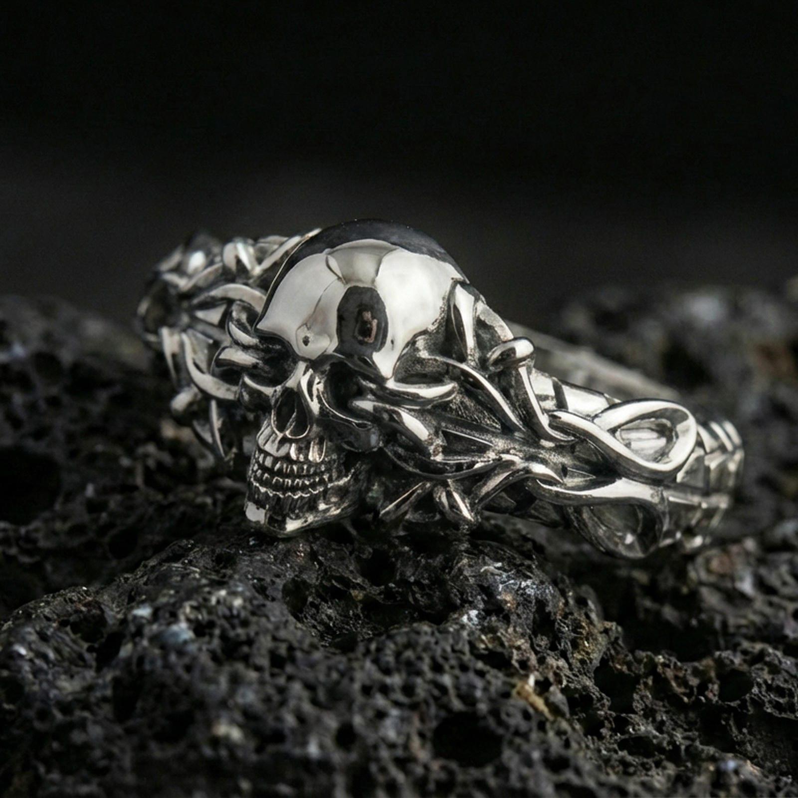 Polished silver skull and vine ring on porous volcanic stone, close-up highlighting bright shine, sharp skull detail and intertwined chain-like branches