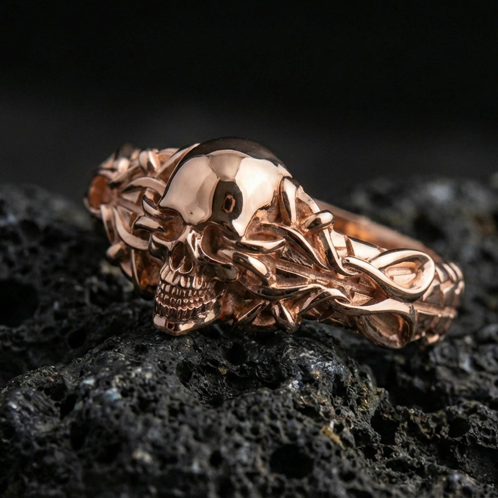 Rose gold plated skull with twisted vine ring on textured volcanic rock, luxury close-up capturing warm plating glow and detailed gothic skull sculpting