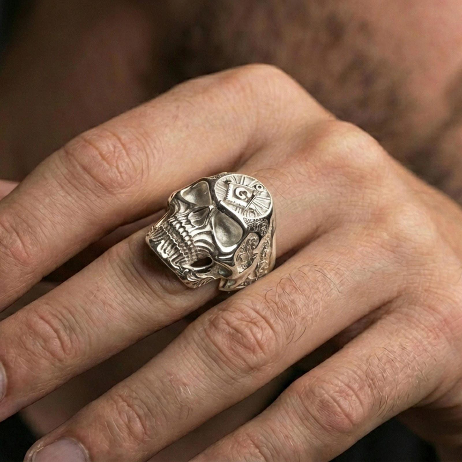 Polished silver skull ring with square and compass “G” symbol worn on the finger, wearable shot showing reflective finish and crisp carving