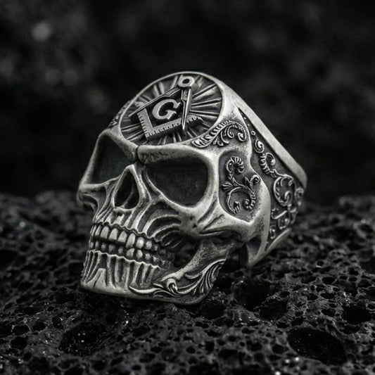 Oxidized sterling silver skull ring with Masonic square and compass “G” emblem on the crown, on black volcanic rock in a dark macro studio shot