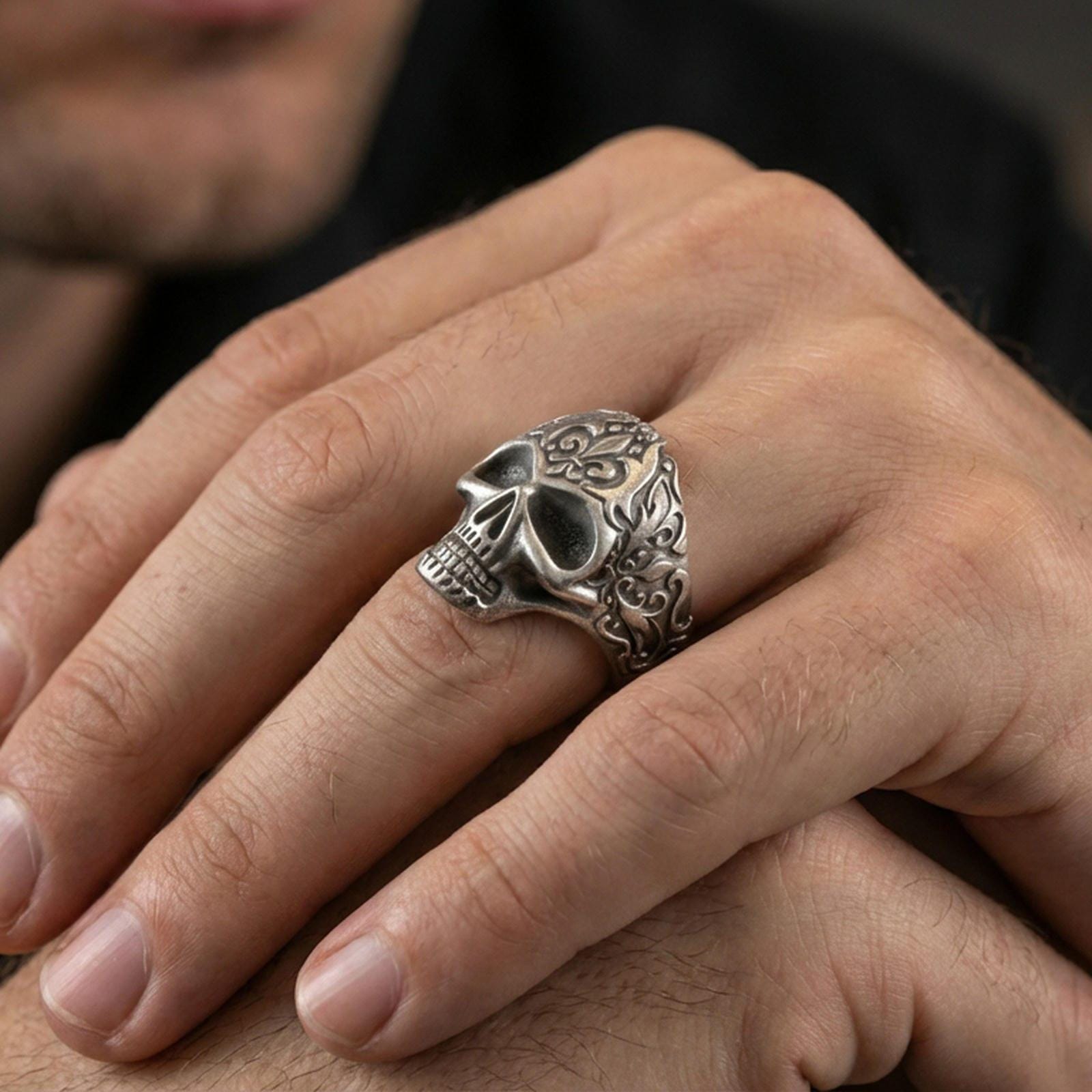 Oxidized filigree skull ring worn on a finger, close-up lifestyle shot showing deep shadows in the eye sockets and engraved scrollwork sides