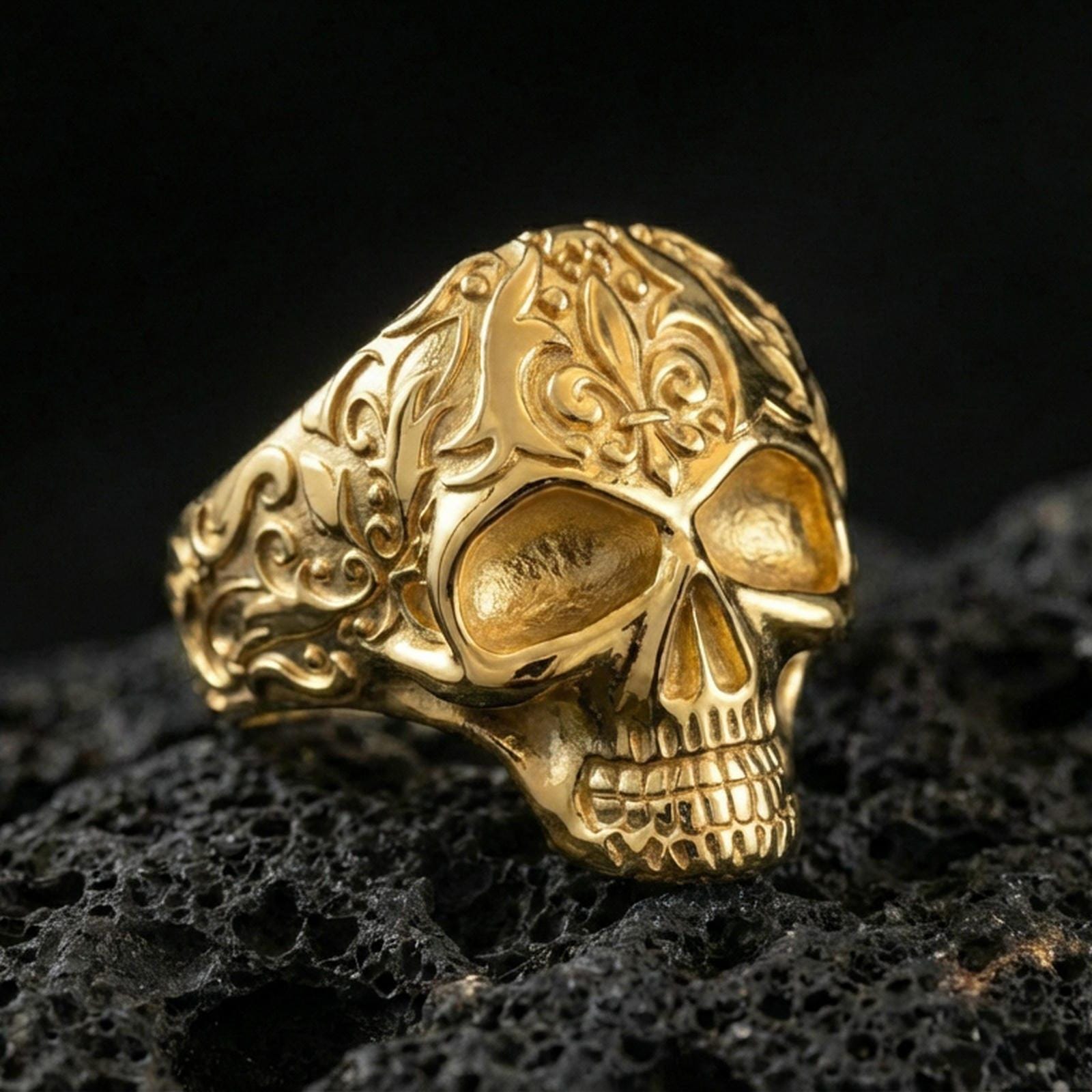 Gold plated ornate skull ring with baroque-style filigree engraving on the band, product photo on porous volcanic rock under dramatic lighting