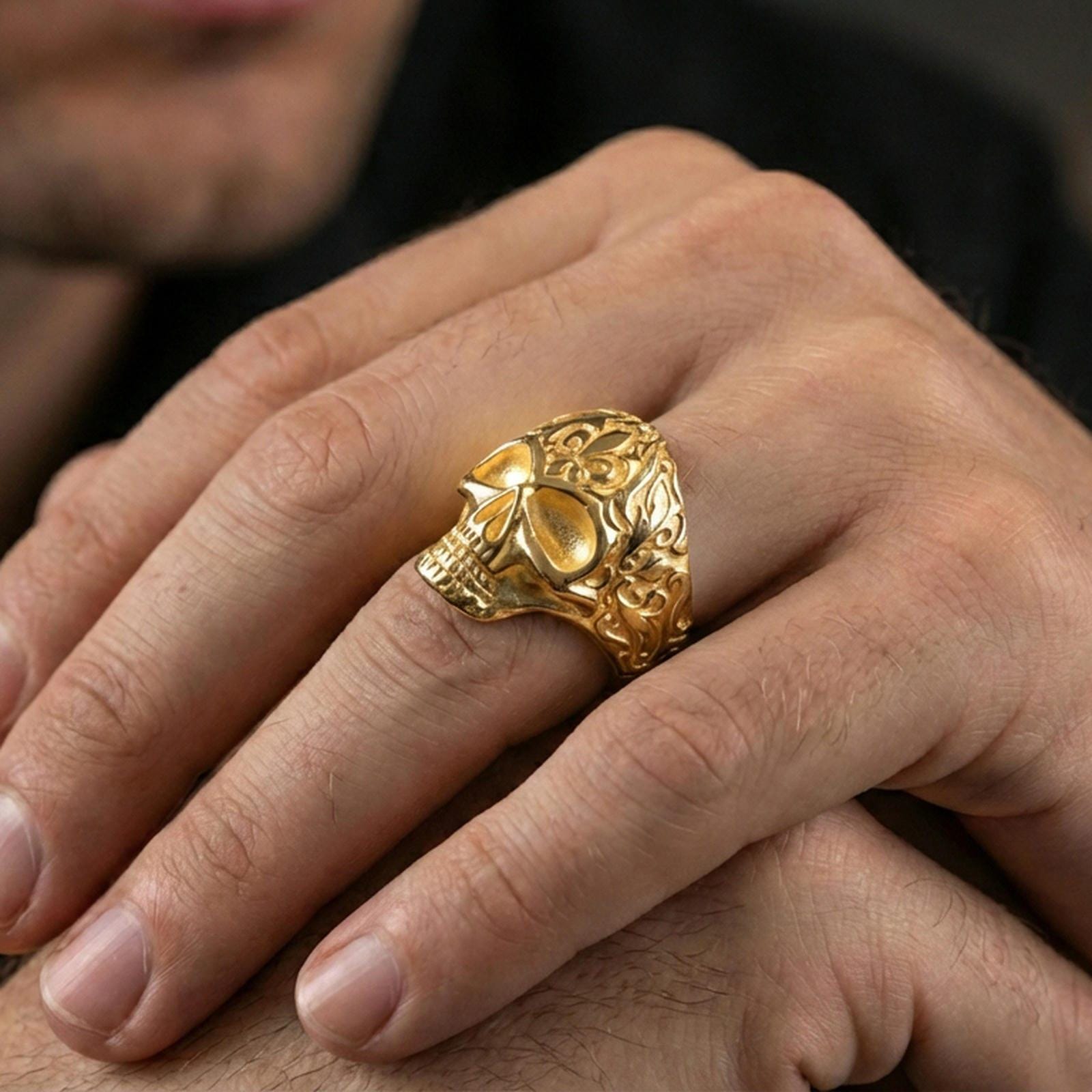 Gold plated skull ring with baroque scrollwork worn on a finger, lifestyle image emphasizing warm tone and bold gothic statement look