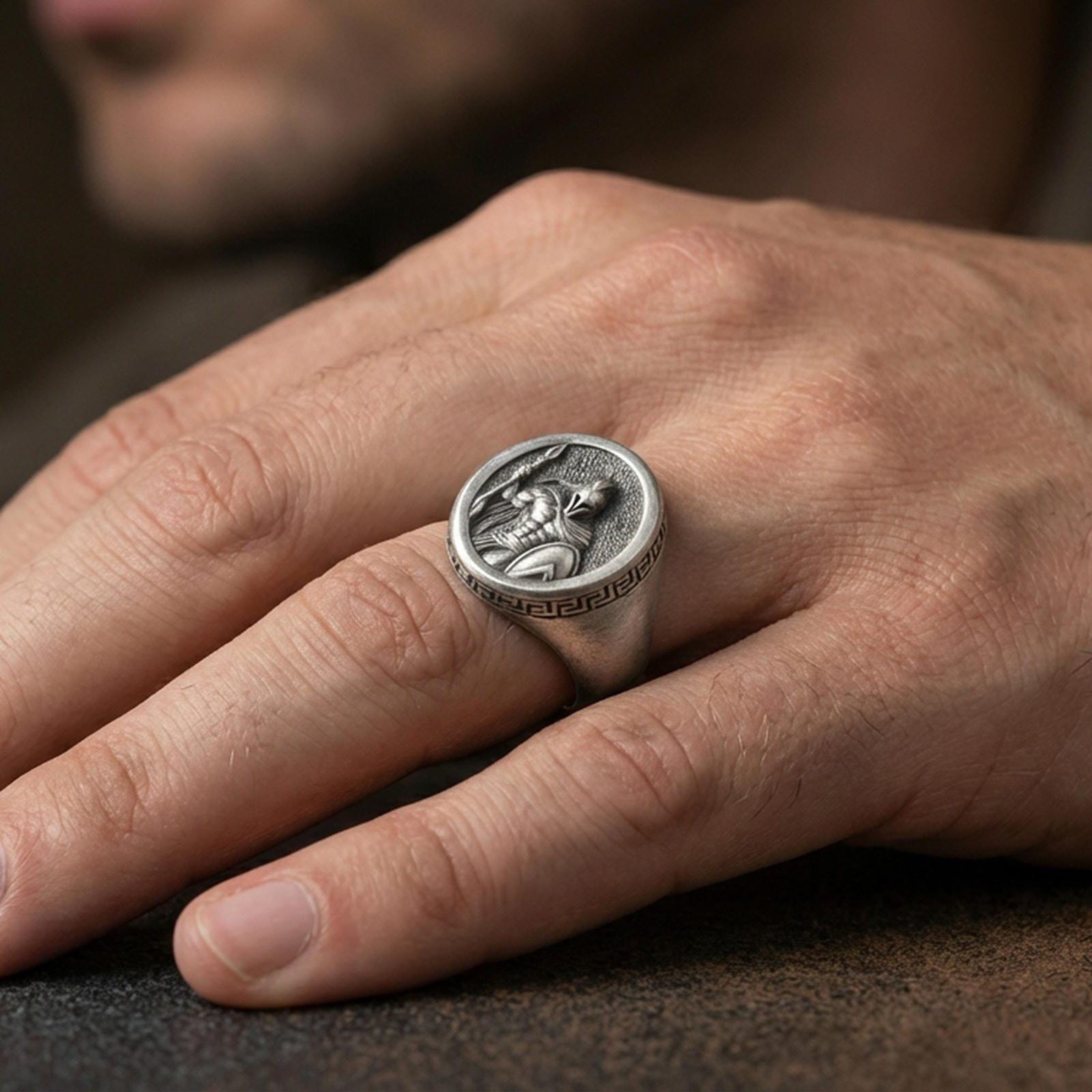 Oxidized Spartan warrior signet ring worn on a finger, close-up lifestyle shot showing deep relief and Greek key side pattern